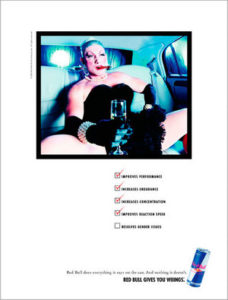 Red bull progressive gender-neutral campaign. Person sitting in back seat of car in black dress holding a glass of Champagne